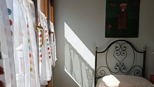 A bedroom with a bed, a radiator, a window with curtains, and a painting on the wall.