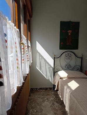 A bedroom with a bed, a radiator, a window with curtains, and a painting on the wall.