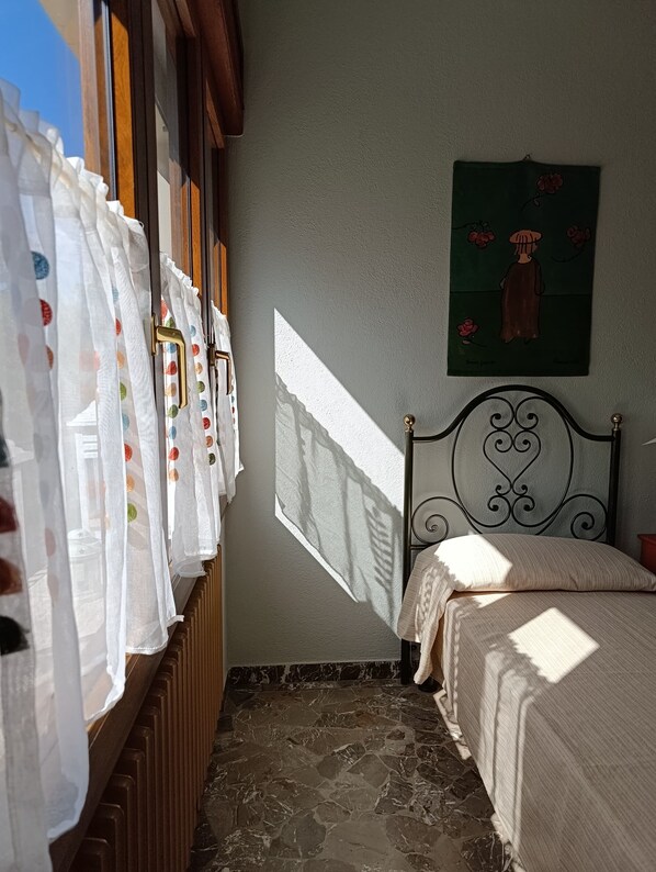A bedroom with a bed, a radiator, a window with curtains, and a painting on the wall.