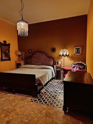 Una camera da letto con un letto, un comodino, una cassettiera, uno specchio, un lampadario e un pavimento decorato.