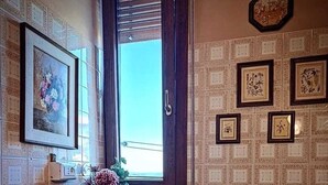 Casa de banho com sanita, lavatório com um vaso de flores, janela e azulejos estampados.