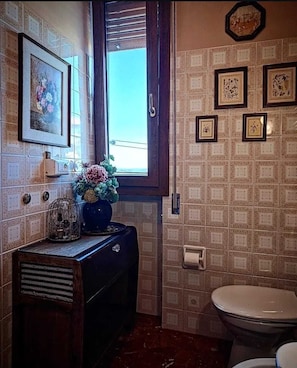Un bagno con il water, un lavabo con un vaso di fiori, una finestra e piastrelle decorate.