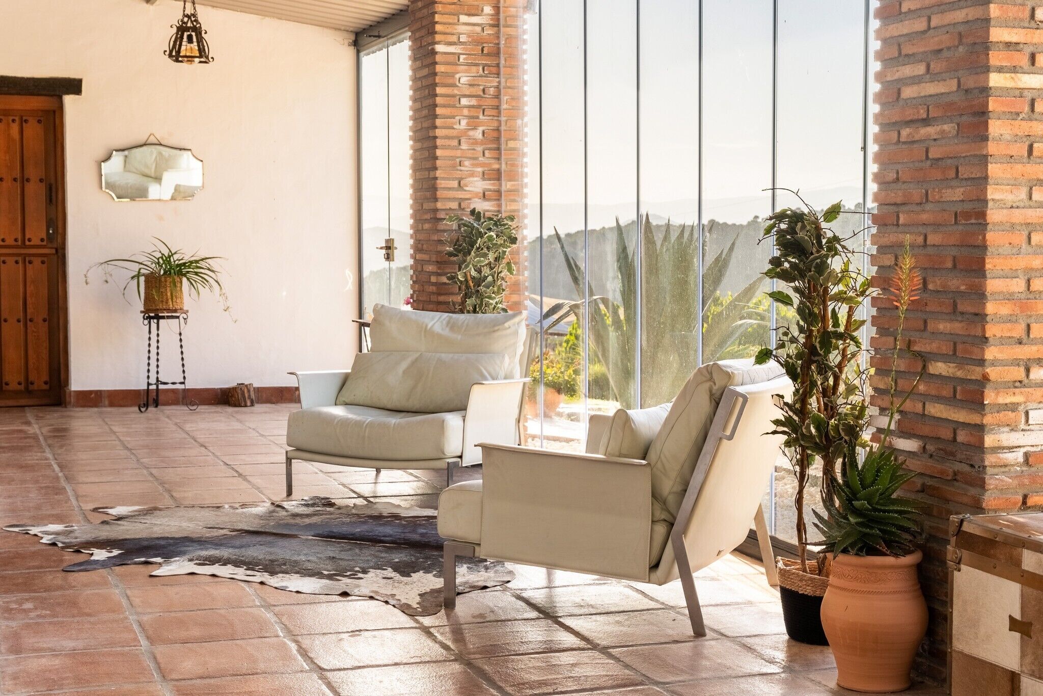 A spacious patio with two leather sofas, a rustic rug, and potted plants.