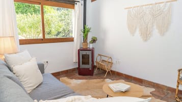 Una habitación acogedora con sofá, una mesita, calefacción y una ventana con cortinas.