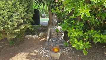 Una estatua de una figura sentada en un jardín con follaje circundante y un pequeño recipiente de ofrendas.