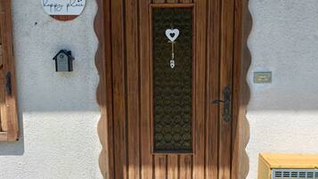 Una puerta de madera con un ventanal en forma de corazón, un felpudo con la palabra 'Hello' y un diseño floral, y una placa con el número 14 en la pared.