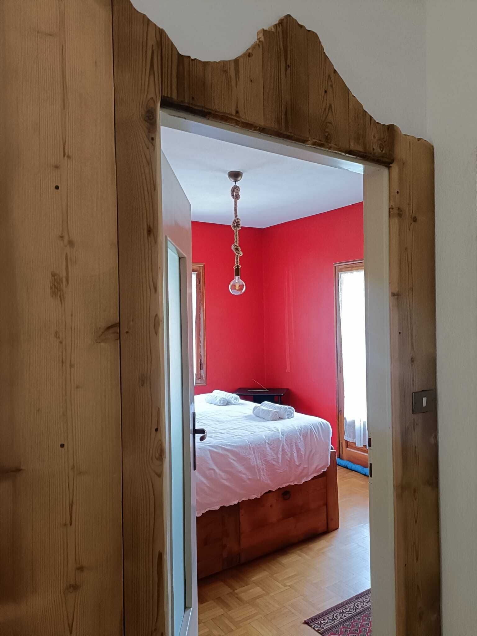Una habitación con una cama, una lámpara colgante y una pared roja.