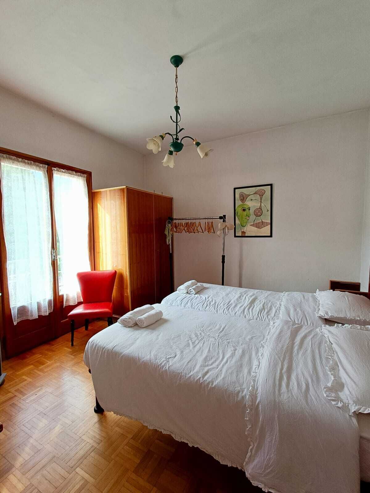 A hotel room with a large bed, a red chair, a wooden wardrobe, and a painting on the wall.