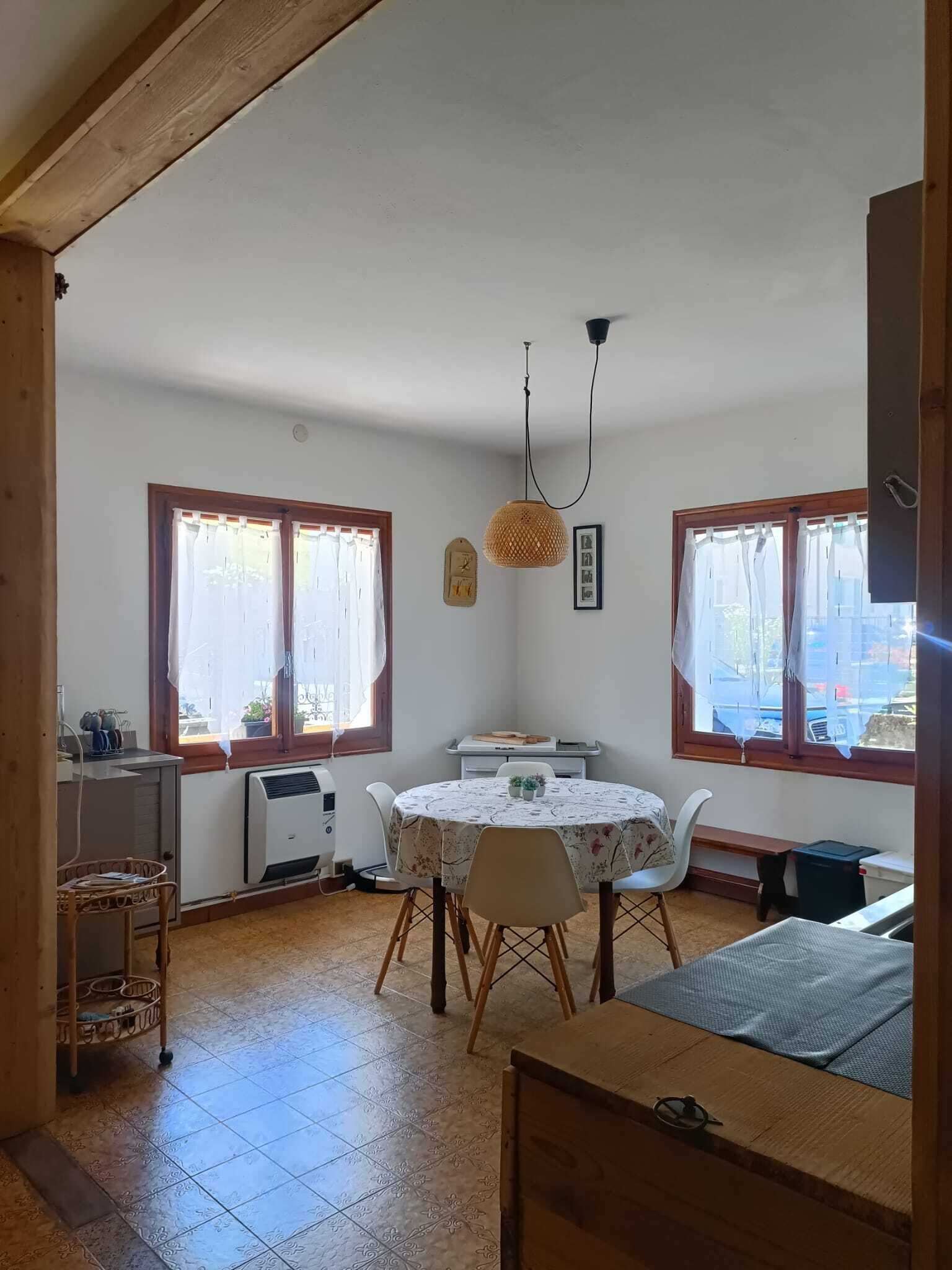 Una habitación con una mesa de comedor, sillas, una lámpara colgante y ventanas con cortinas.