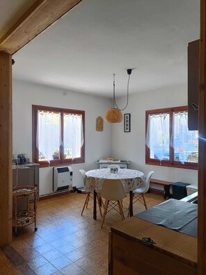Una habitación con una mesa de comedor, sillas, una lámpara colgante y ventanas con cortinas.