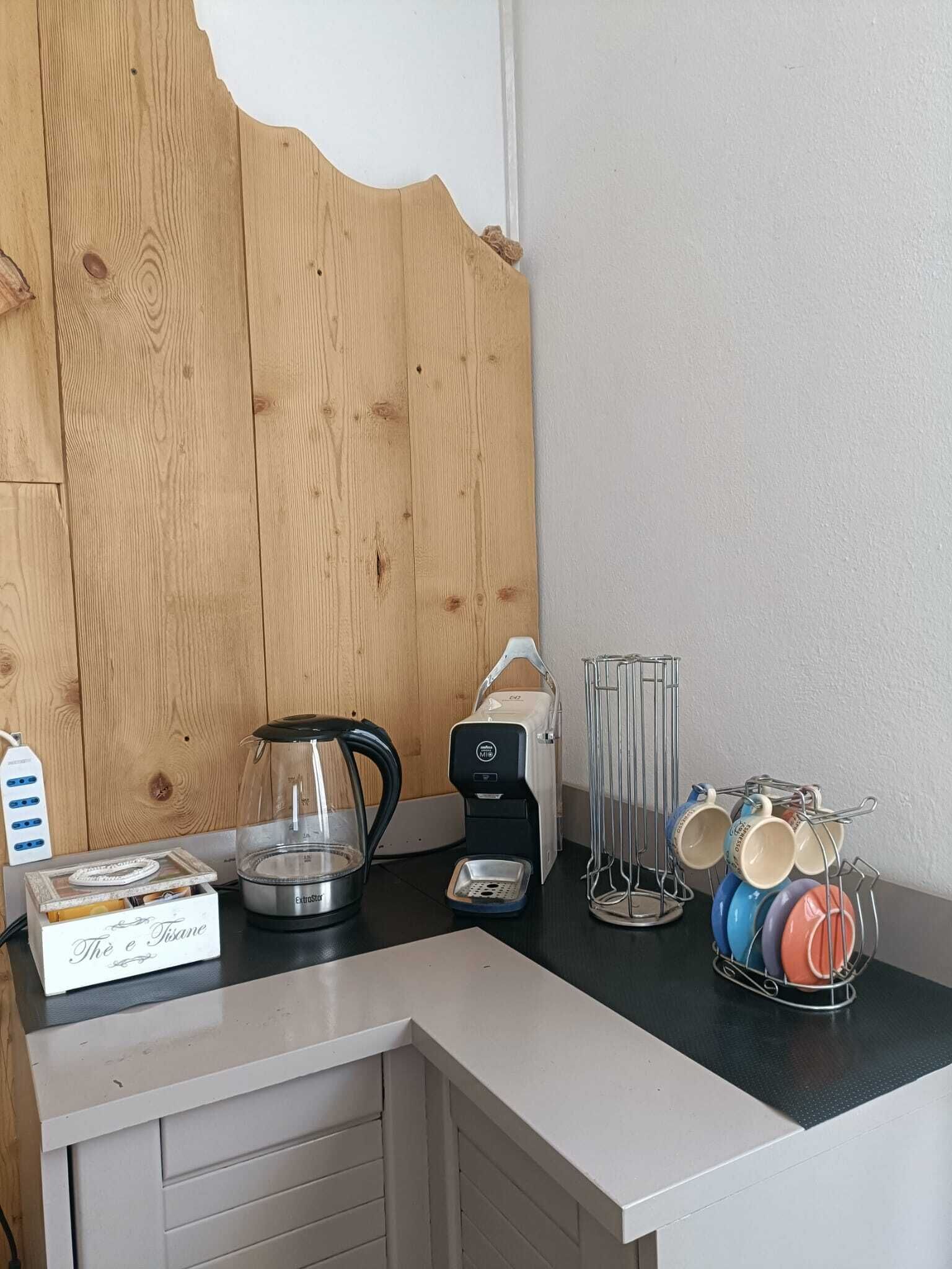 Ett litet kök med en kaffebryggare, en glaskanna, en låda märkt ”Te och örtte” och ett ställ för kaffemuggar.