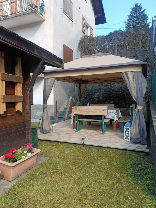 A covered outdoor seating area with a table and chairs, a wooden bench, and a flower pot.