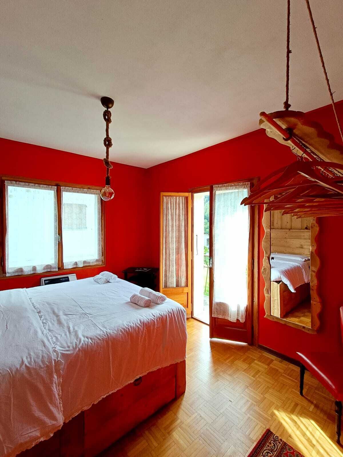 Una camera da letto con un letto, un pavimento in legno, una parete rossa e una finestra.