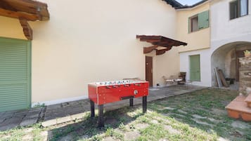 Uma mesa de futebol de brinquedo vermelha em um pátio com piso de pedra, pérgola de madeira e um edifício com persianas verdes.