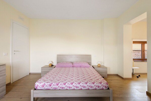 Une chambre avec un lit simple, deux tables de chevet, une armoire et une fenêtre avec des stores.