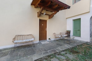 A stone-paved patio with wicker furniture, a wooden door, and a green shuttered window. - Relaxing Room Surrounded by Nature (Pontremoli)