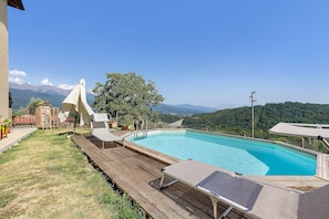 A swimming pool with a wooden deck and lounge chairs, surrounded by a mountainous landscape. - Relaxing Room Surrounded by Nature (Pontremoli)