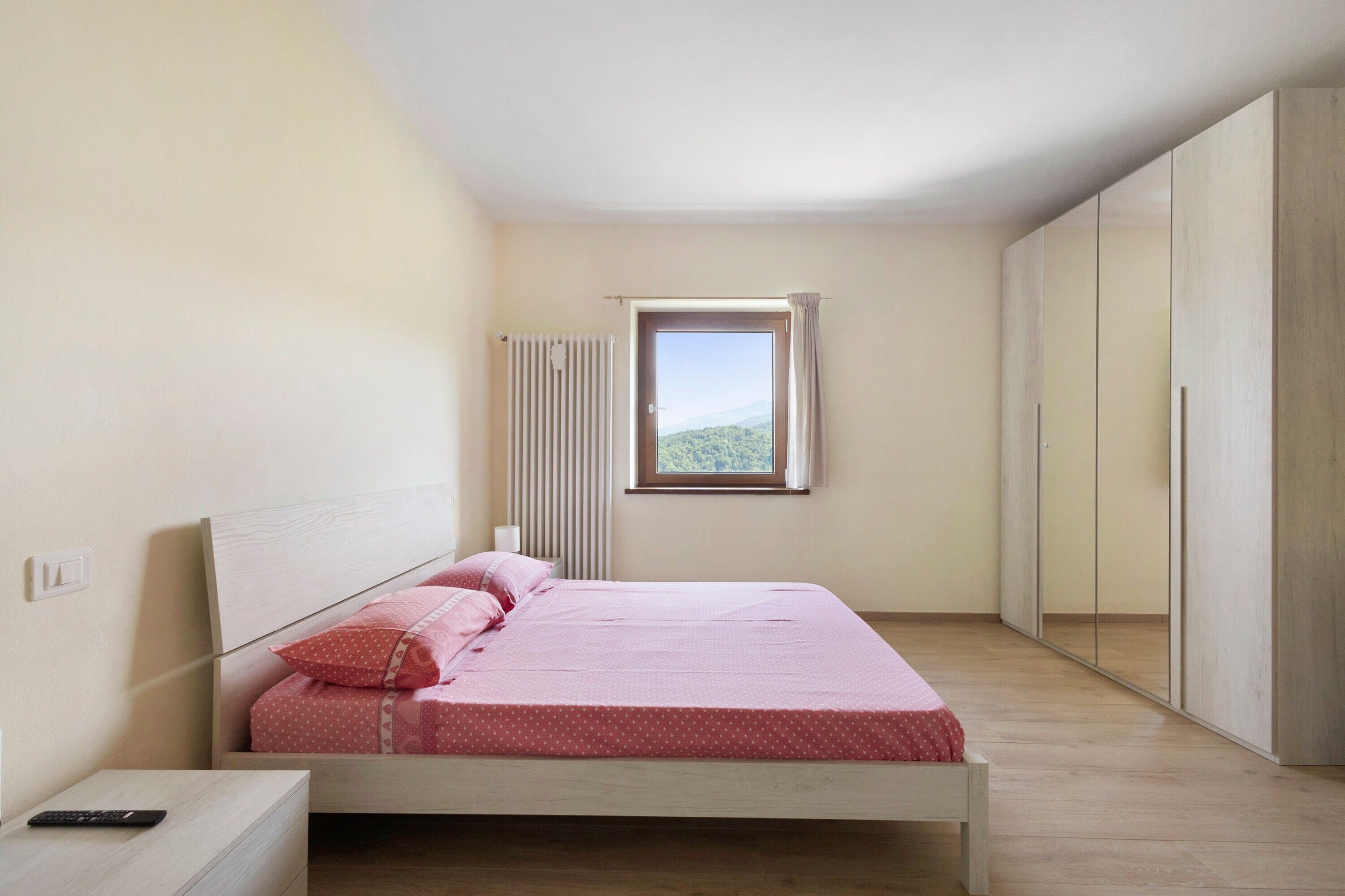 Un dormitorio con cama, mesita de noche, ventana con vistas y armario.