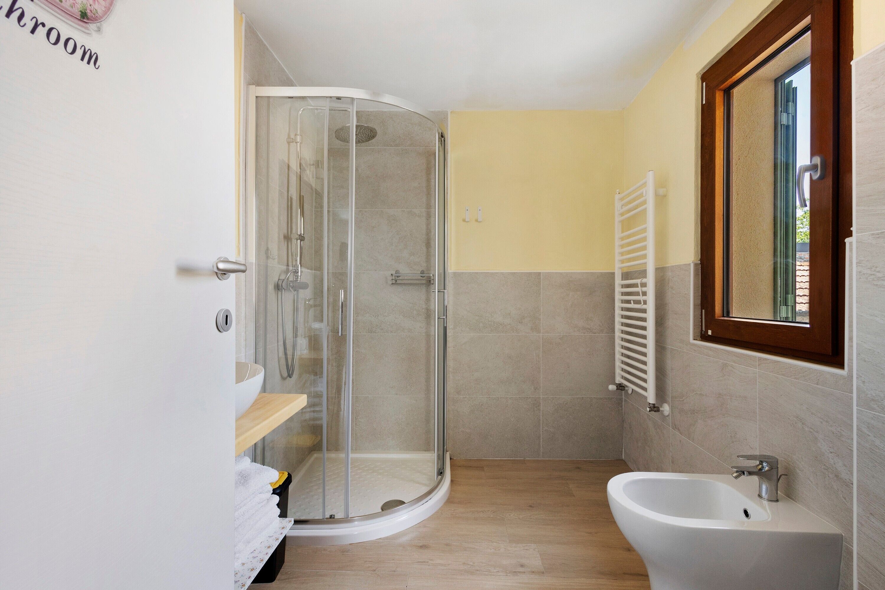 A bathroom with a glass-enclosed shower, a sink, and a window.