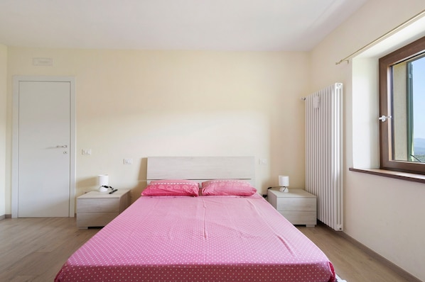 A bedroom with a bed, bedside tables, a radiator, a window, and a door. - Relaxing Room Surrounded by Nature (Pontremoli)