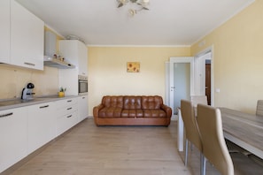 A compact living space with a kitchenette, a brown leather sofa, a dining table with chairs, and a door leading to another room. - Relaxing Room Surrounded by Nature (Pontremoli)