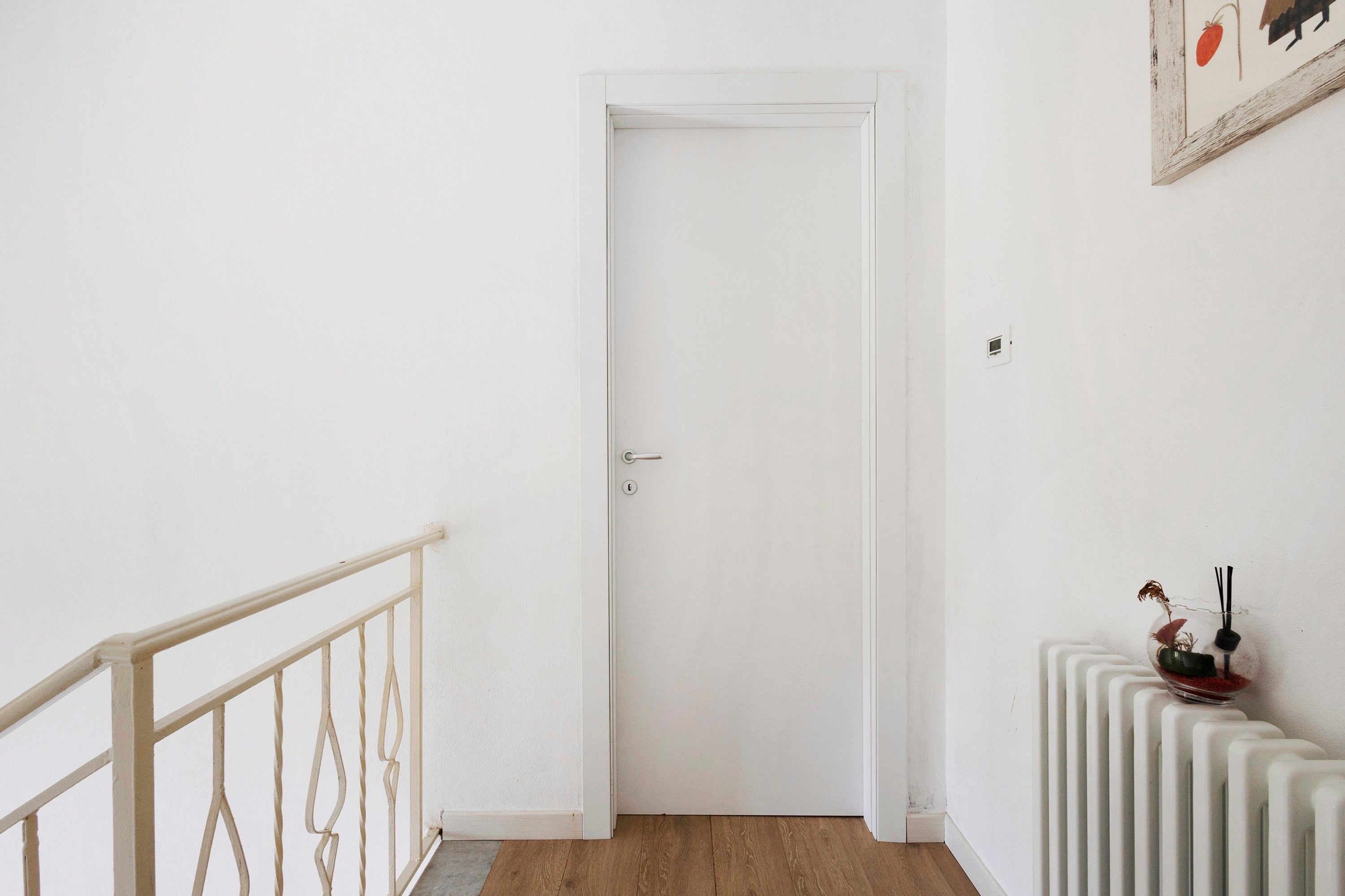 Una puerta blanca con un pomo sencillo, un radiador blanco y una pequeña mesa con una planta y una vela.