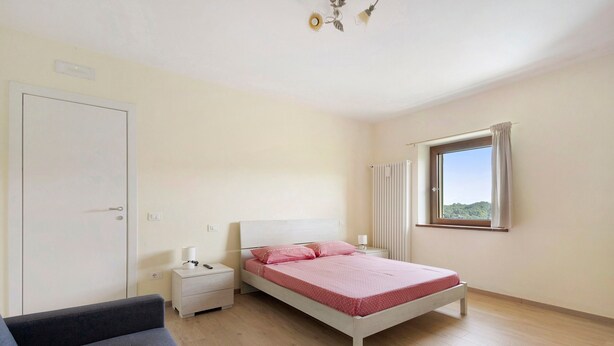 Une chambre à coucher avec un lit, une table de chevet, une chaise, une fenêtre et un radiateur.