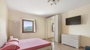 Une chambre à coucher comprenant un lit, une commode, un téléviseur et une fenêtre donnant sur l’extérieur.