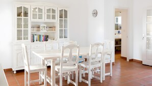 A dining area with a white table and chairs, a white cabinet with glass doors, and a clock on the wall.