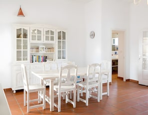 A dining area with a white table and chairs, a white cabinet with glass doors, and a clock on the wall.