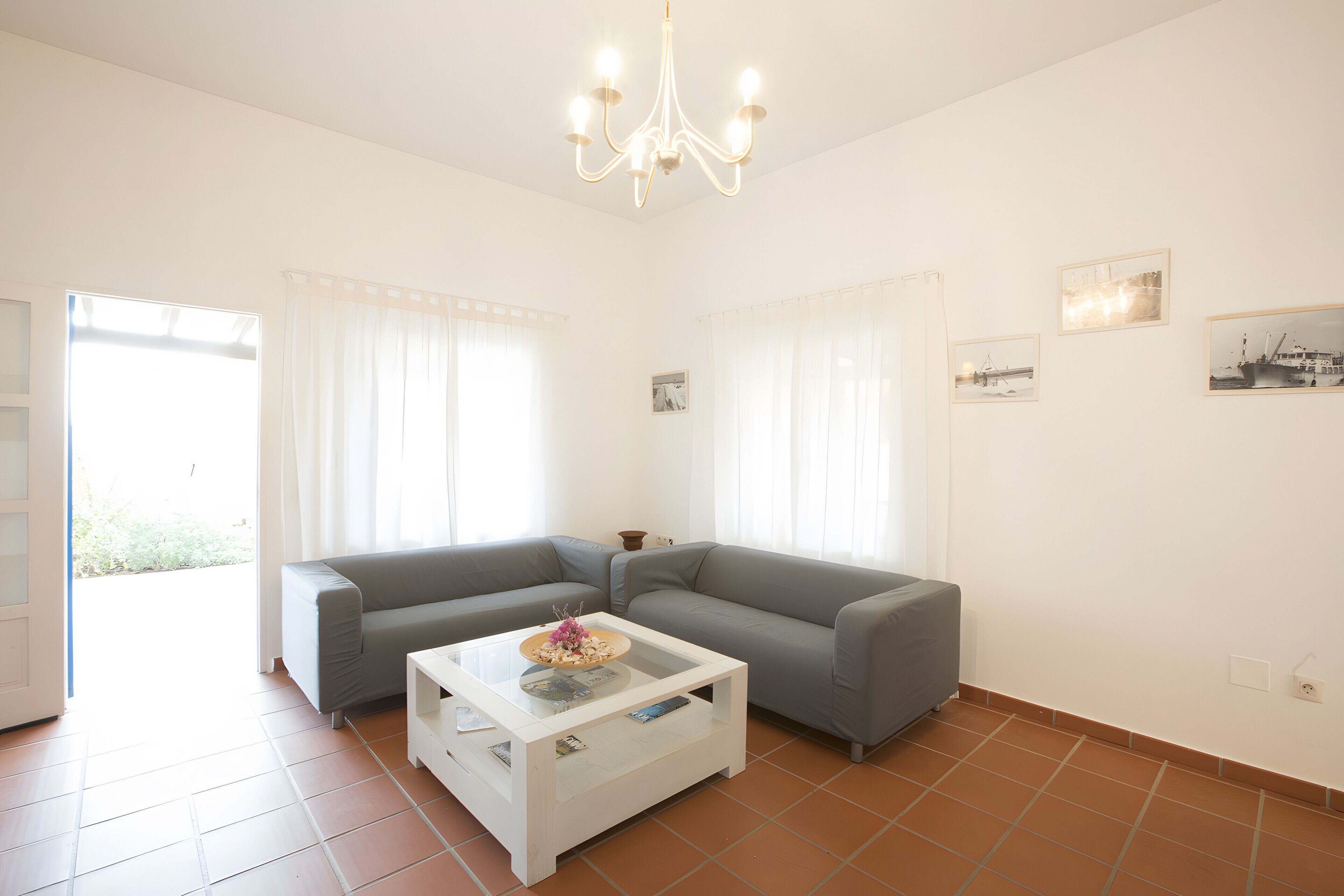 Una sala de estar moderna con un sofá gris, una mesa de centro blanca y una araña.