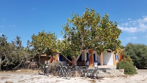 A building with a covered outdoor seating area, a bicycle parked in front, and a clear blue sky. - Casa Rita in Formentera with Sea Views (Sant Ferran de ses Roques)