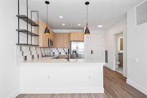 A modern kitchen with a central island, pendant lighting, and a view into the adjacent bathroom. - Modern Huntsville Stay | 1 Unit | Central Location (Huntsville)