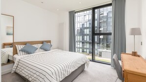 Een moderne hotelkamer met een groot bed, een bureau en uitzicht op de stad door middel van kamerhoge ramen.