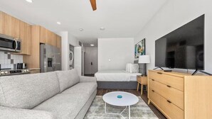 Ein modernes Hotelzimmer mit einer Küchenzeile, einem Sofa, einem Bett, einem Fernseher und einem kleinen Tisch.