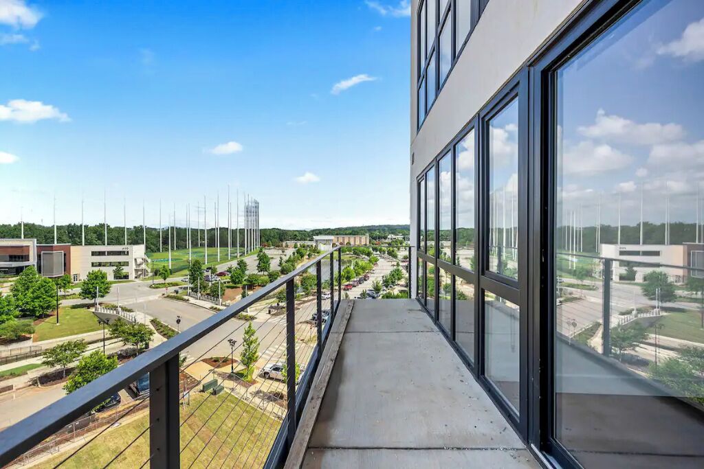 Ein Balkon mit freiem Blick auf einen Parkplatz, Gebäude und Grünflächen.