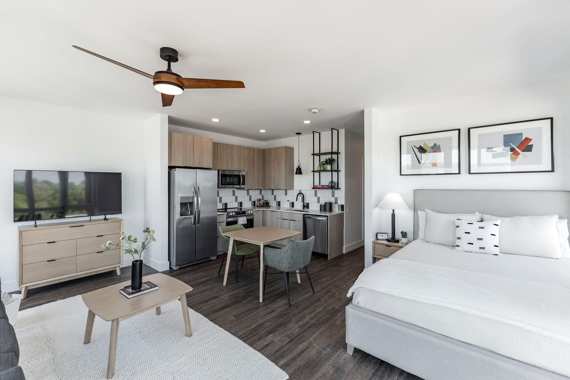 Ein modernes Hotelzimmer mit Bett, Schreibtisch, Küchenzeile und Fernseher.