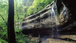 Eine natürliche Felsformation mit einem Wasserfall in bewaldeter Landschaft.