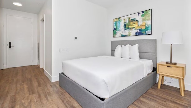 Ein Hotelzimmer mit Bett, Nachttisch und einem an der Wand hängenden abstrakten Gemälde.