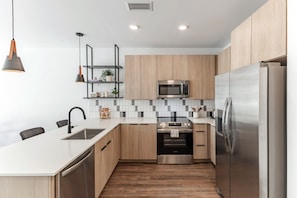 A modern kitchen with wooden cabinets, a stainless steel refrigerator, a built-in oven, a microwave, and a pendant light. - Modern Huntsville Stay | 1 Unit | Near Mid City Drive (Huntsville)