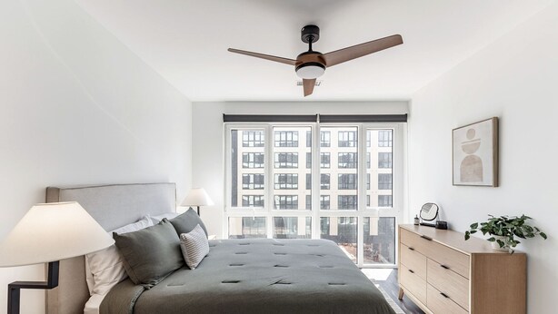 Ein Schlafzimmer mit Bett, Nachttischlampe, Kommode und Deckenventilator.