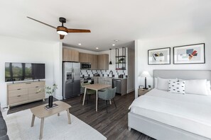 Una habitación de hotel moderna con cama, escritorio, kitchenette y televisor.