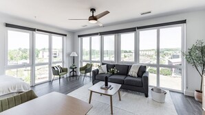 Un salón amplio con ventanas grandes, un ventilador de techo, un sofá, una mesa de centro y una mesita auxiliar.