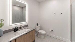 Un baño moderno con un espejo grande, un lavamanos, un inodoro y una zona de ducha.