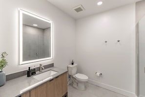 Ein modernes Badezimmer mit großem Spiegel, Waschbecken, Toilette und Duschbereich.