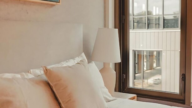 A hotel room with a bed, pillows, a lamp, and a window with a view of buildings. - Modern Atlanta Retreat | Deluxe City View room | Near Midtown Hotspots (Atlanta)