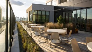 Eine Terrasse im Freien mit runden Tischen und Stühlen, einem Holzboden und Blick auf die Stadtlandschaft.