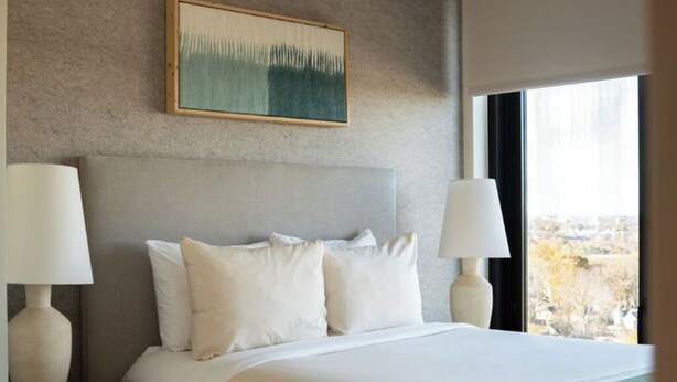 A hotel room with a bed, two bedside lamps, a painting on the wall, and a window with a view. - Deluxe One Bedroom City View Near Midtown District (Atlanta)
