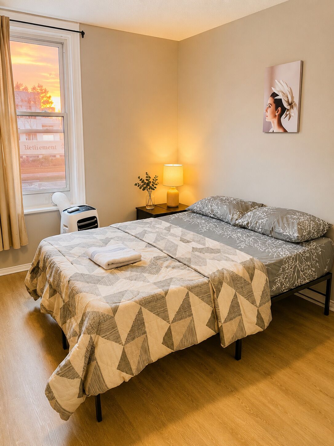 A neatly made bed with a patterned bedspread, a bedside lamp, and a small table with a vase of flowers.