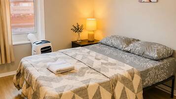 A neatly made bed with a patterned bedspread, a bedside lamp, and a small table with a vase of flowers.